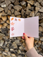 illustrated fall leaves greeting card held up by a hand with wooden background. 