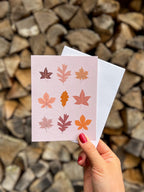 illustrated fall leaves greeting card held up by a hand with wooden background. 