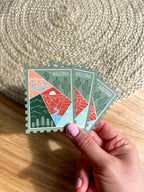 Colorful postage stamp design of Arizona held by a hand against a textured fabric background