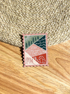 A magnet shaped like a postage stamp with an illustration of the Utah state, placed on a wooden surface.