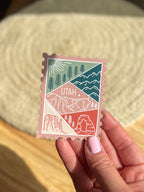 A magnet shaped like a postage stamp with an illustration of the Utah state, held by hand