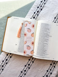 Open book with a Christian bookmark featuring peach illustrations on a textured fabric surface. verse Psalm 150:6