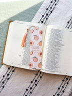 Open book with a Christian bookmark featuring peach illustrations on a textured fabric surface. verse Psalm 150:6