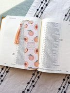 Open book with a decorative bookmark featuring peach illustrations on a textured fabric background.