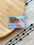 Stylized postage stamp magnet of Connecticut on a textured surface with wooden and fabric elements.