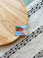 Stylized postage stamp magnet of Connecticut on a textured surface with wooden and fabric elements.