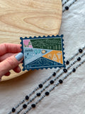 holding a Colorful Washington stamp-shaped magnet on a textured fabric background