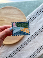 holding a Colorful Washington stamp-shaped magnet on a textured fabric background