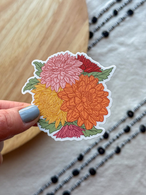 illustrated Chrysanthemums sticker held by a hand with light blue nail polish on a textured surface.