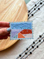 Colorful Colorado-themed stamp magnet on a wooden surface 