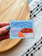 Colorful Colorado-themed stamp magnet on a wooden surface 