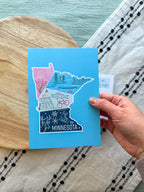 Colorful Minnesota-themed postcard on a textured surface