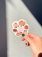 A vinyl sticker with a design of pumpkins, leaves, and the text 'THANKFUL & BLESSED' hand hold it up