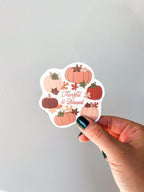 A vinyl sticker with a design of pumpkins, leaves, and the text 'THANKFUL & BLESSED' hand hold it up