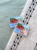 Two decorative postage stamp-shaped stickers on a textured surface with a blurred background.