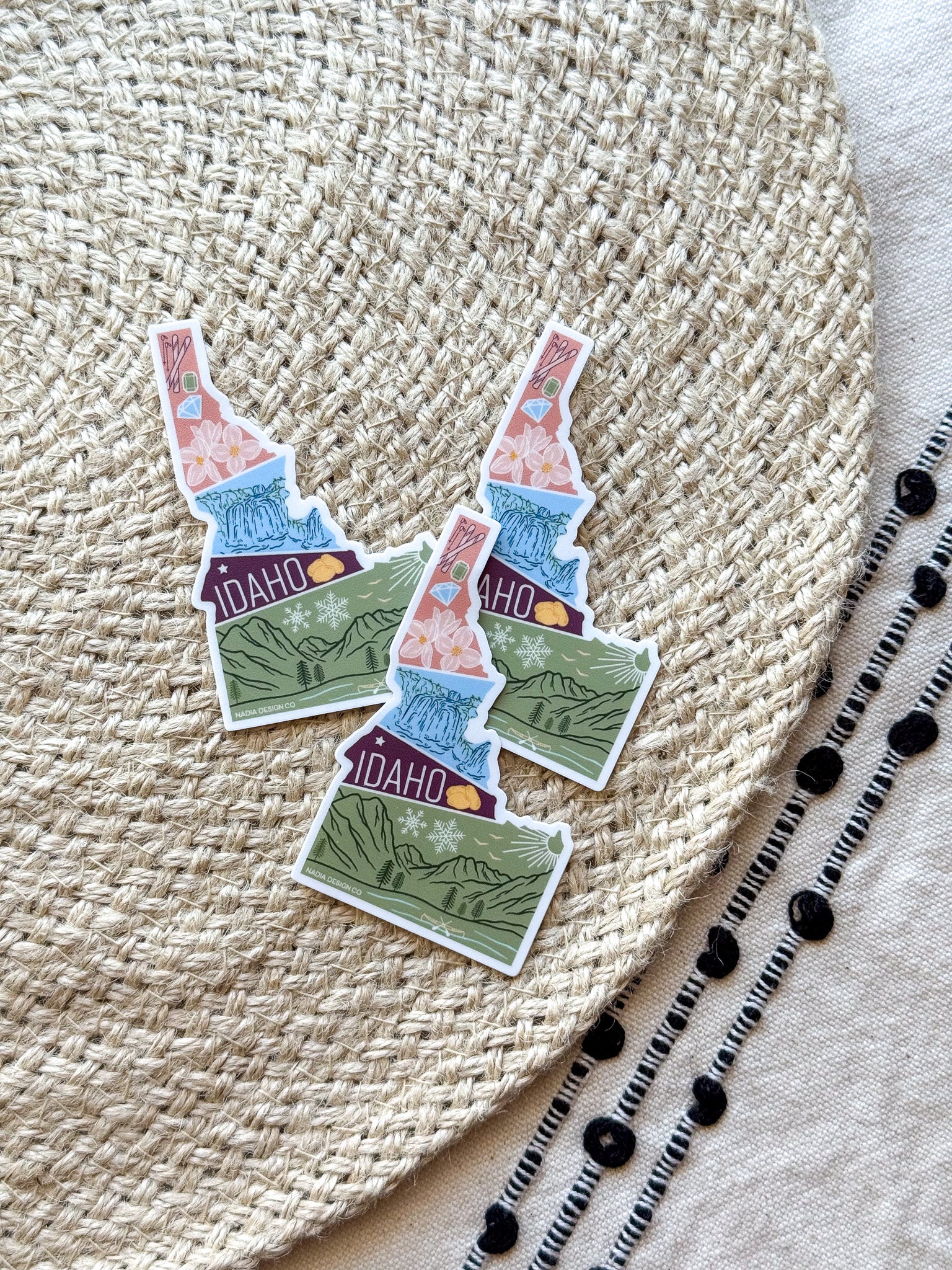 sticker of Idaho with scenic illustrations  on a textured fabric background