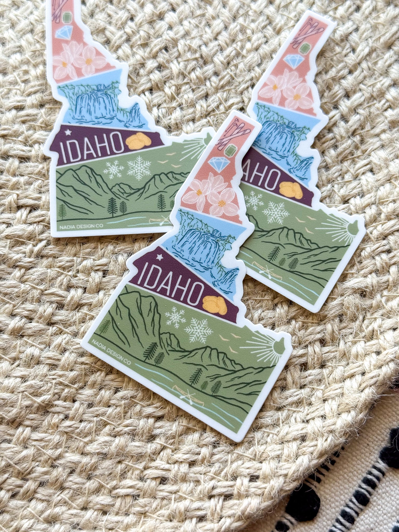 sticker of Idaho with scenic illustrations stamp design held by a hand on a textured fabric background