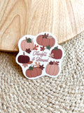 A vinyl sticker with a design of pumpkins, leaves, and the text 'THANKFUL & BLESSED' on a wooden surface.