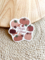 A vinyl sticker with a design of pumpkins, leaves, and the text 'THANKFUL & BLESSED' on a wooden surface.
