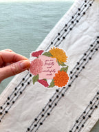 Hand holding a floral sticker with text on a textured fabric background