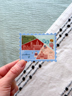 Connecticut Postcard featuring a colorful illustration of a map and buildings, nature themed on a blue background, set against a textured fabric surface.