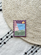 sticker of Idaho with scenic illustrations stamp design held by a hand on a textured fabric background