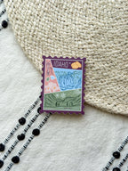sticker of Idaho with scenic illustrations stamp design held by a hand on a textured fabric background