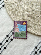 sticker of Idaho with scenic illustrations stamp design held by a hand on a textured fabric background