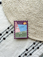 magnet of Idaho with scenic illustrations stamp design held by a hand on a textured fabric background