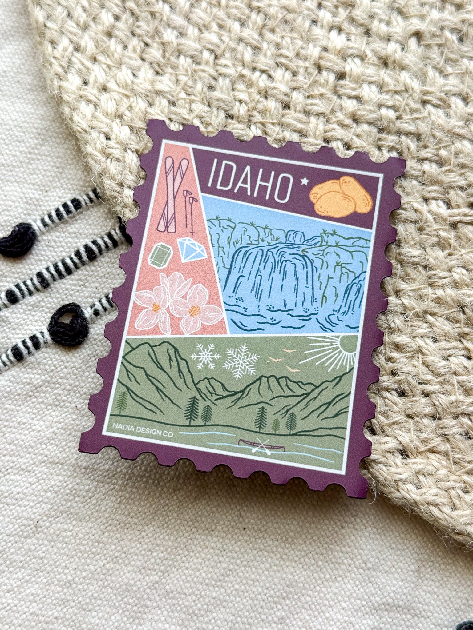 magnet of Idaho with scenic illustrations stamp design held by a hand on a textured fabric background
