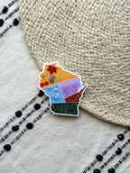 sticker with wisconsin themed illustrations, outline design held by a hand on a textured fabric background