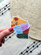 sticker with wisconsin themed illustrations, outline design held by a hand on a textured fabric background