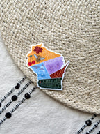 colorful sticker with wisconsin themed illustrations, outline design held by a hand on a textured fabric background