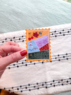 sticker with Wisconsin-themed illustrations, stamp design held by a hand on a textured fabric background