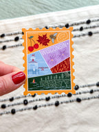 sticker with Wisconsin-themed illustrations, stamp design held by a hand on a textured fabric background