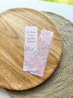 Open book with a pink bookmark featuring floral designs and text "in Christ alone my hope is found" on a woven surface.