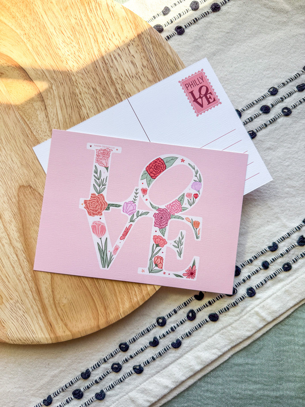 Pink card with floral 'LOVE' design on a wooden surface