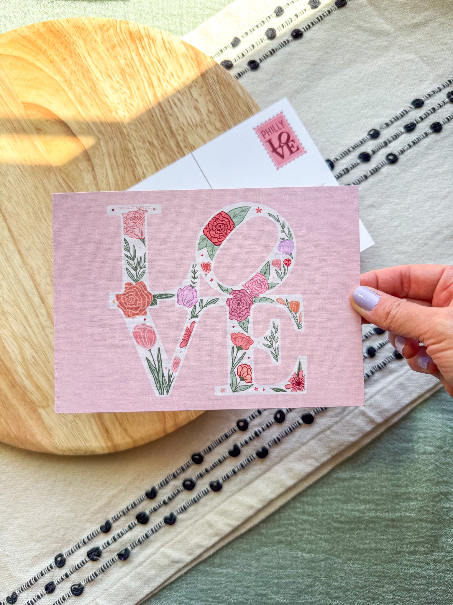 Card with floral 'LOVE' design held by a hand on a wooden surface.