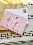Floral 'love' card on a wooden surface with decorative elements.