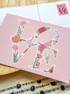 Pink card with floral 'LOVE' design on a wooden surface