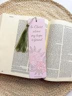 Open book with a pink bookmark featuring floral designs and text "in Christ alone my hope is found" on a woven surface.