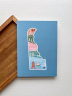 A postcard with an illustration of Delaware state in a colorful artistic style on a blue background.