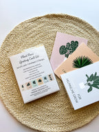 A set of six illustrated greeting cards with various houseplants and punny captions related to plants displayed on a wooden surface.