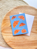 Greeting card with croissant illustrations on a wooden surface