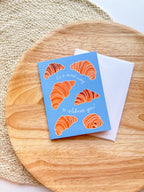 Greeting card with croissant illustrations on a wooden surface