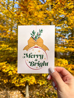 Merry Christmas Card illustrated orenament with bow and greenery. hand holding against yellow trees