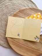 Yellow card with bee and honeycomb design on a wooden surface