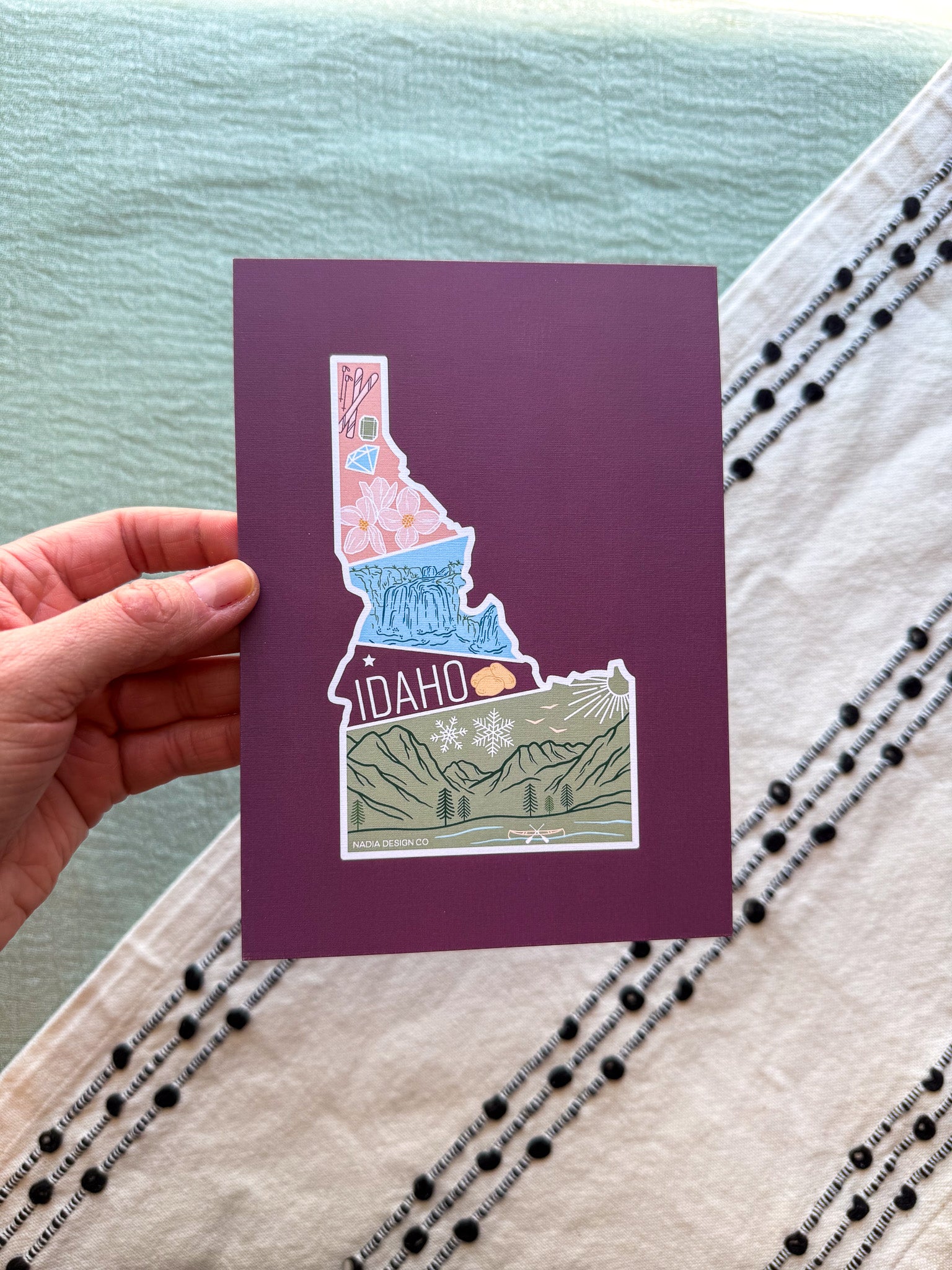 Card with Idaho state design held by a hand on a textured surface