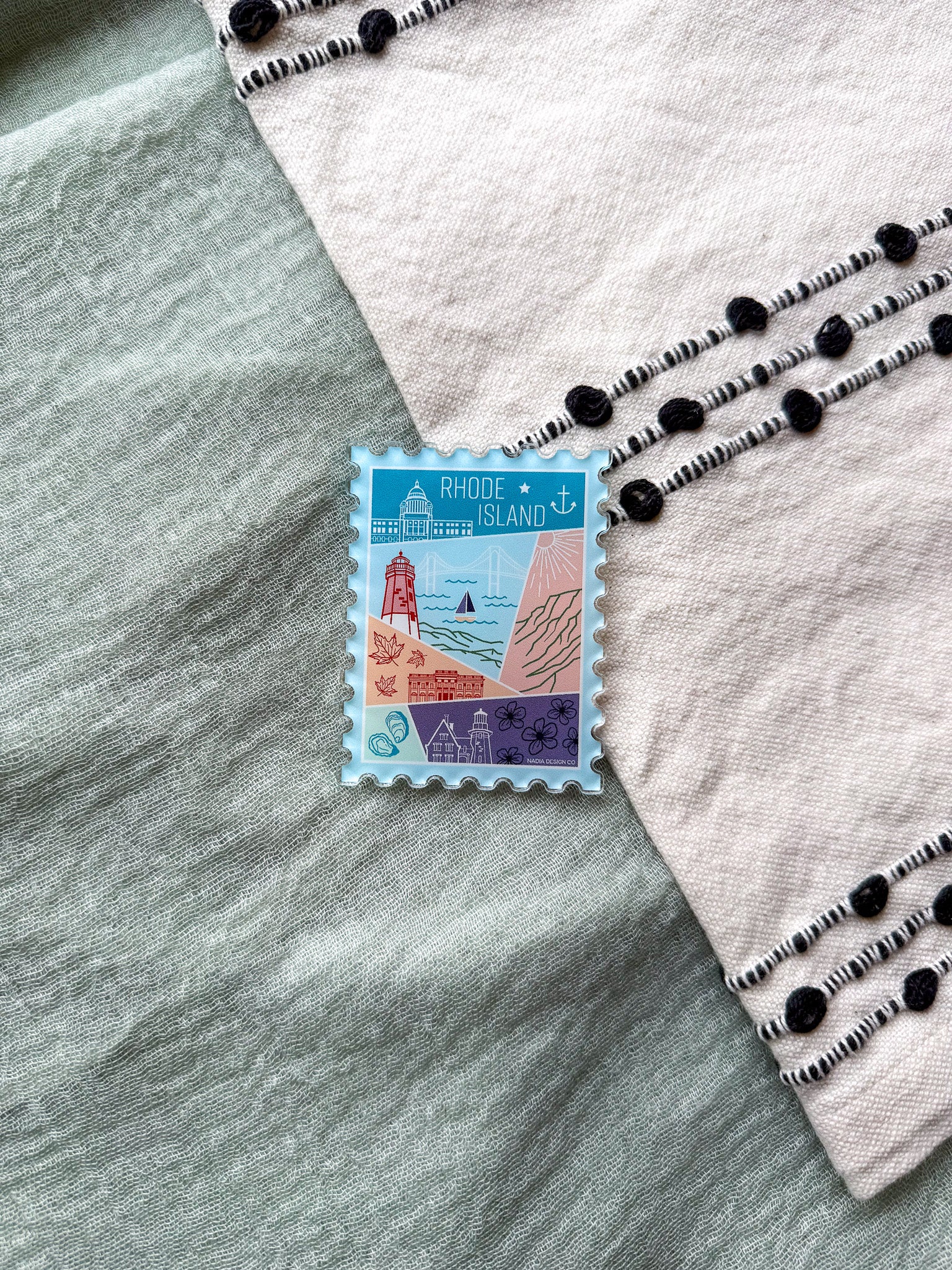 illustrated Rhode Island Acrylic Stamp Magnet held and textured fabric behind