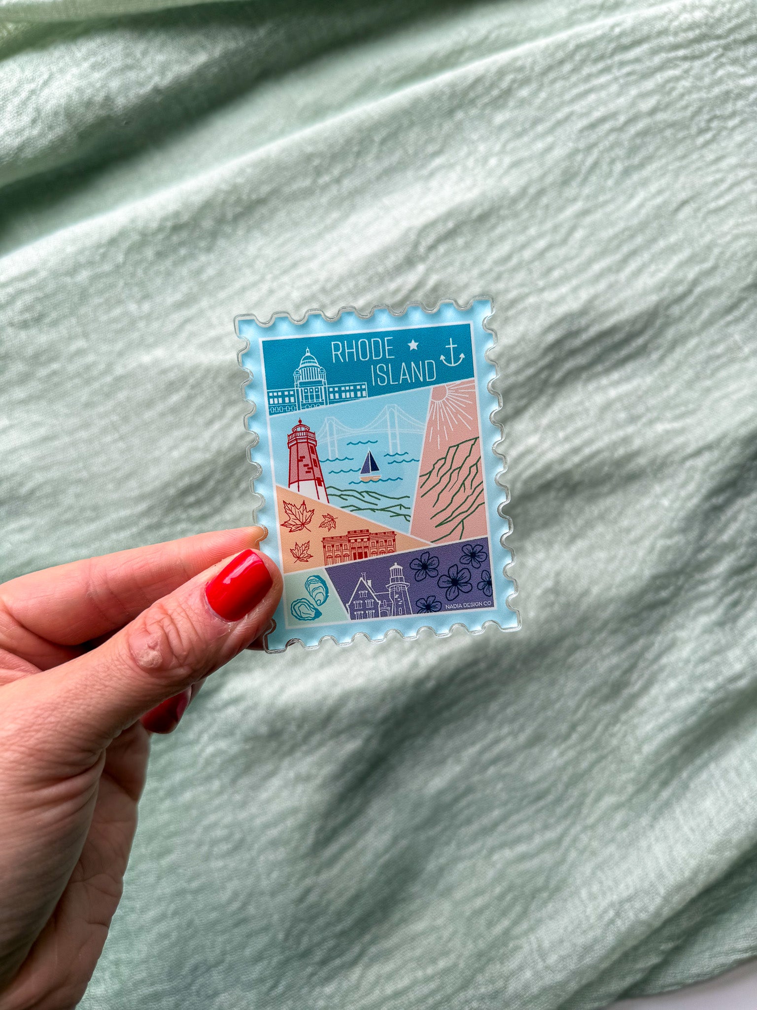 illustrated Rhode Island Acrylic Stamp Magnet held and textured fabric behind